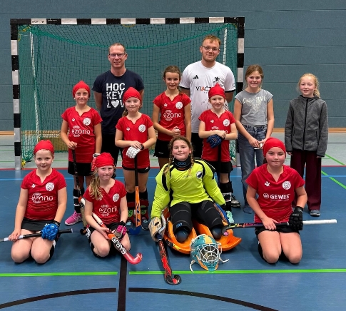 Mannschaftsfoto von Hockeyteam mit Kindern und Erwachsenen in roten Trikots.