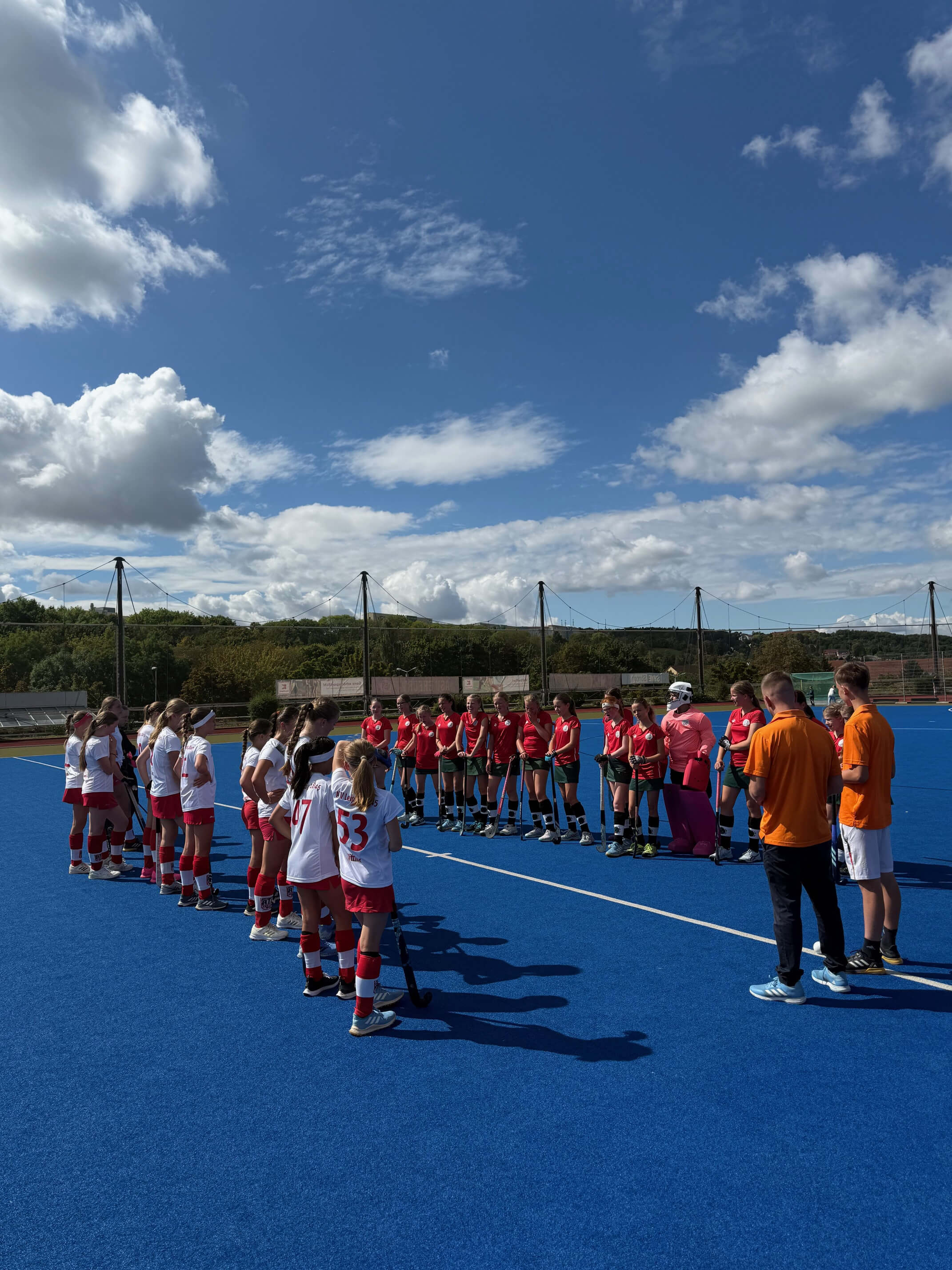 Gruppe von Kindern und Betreuern auf blauem Sportplatz bei sonnigem Wetter