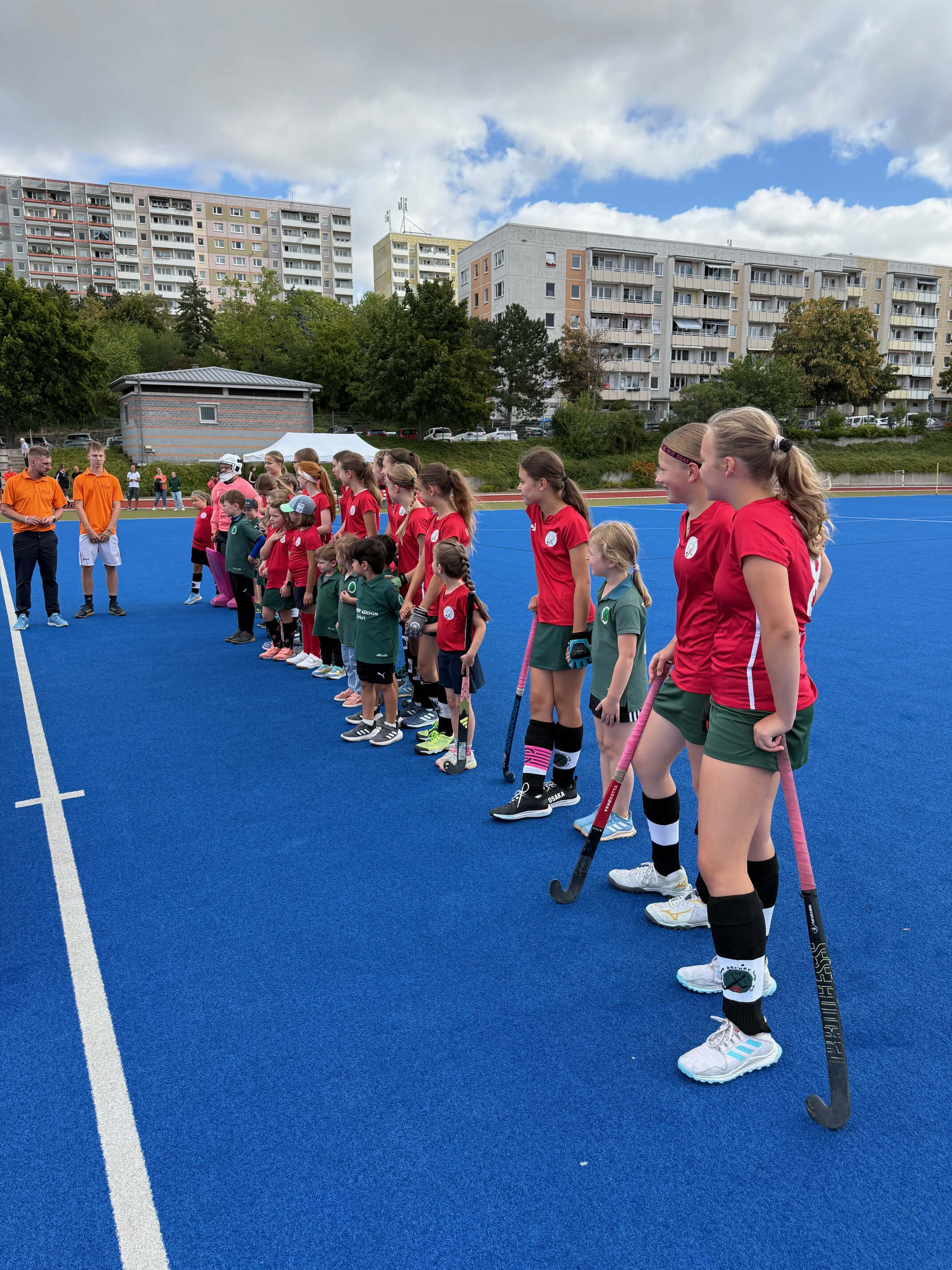 Kinder in roten Trikots laufen auf einem blauen Hockeyfeld.