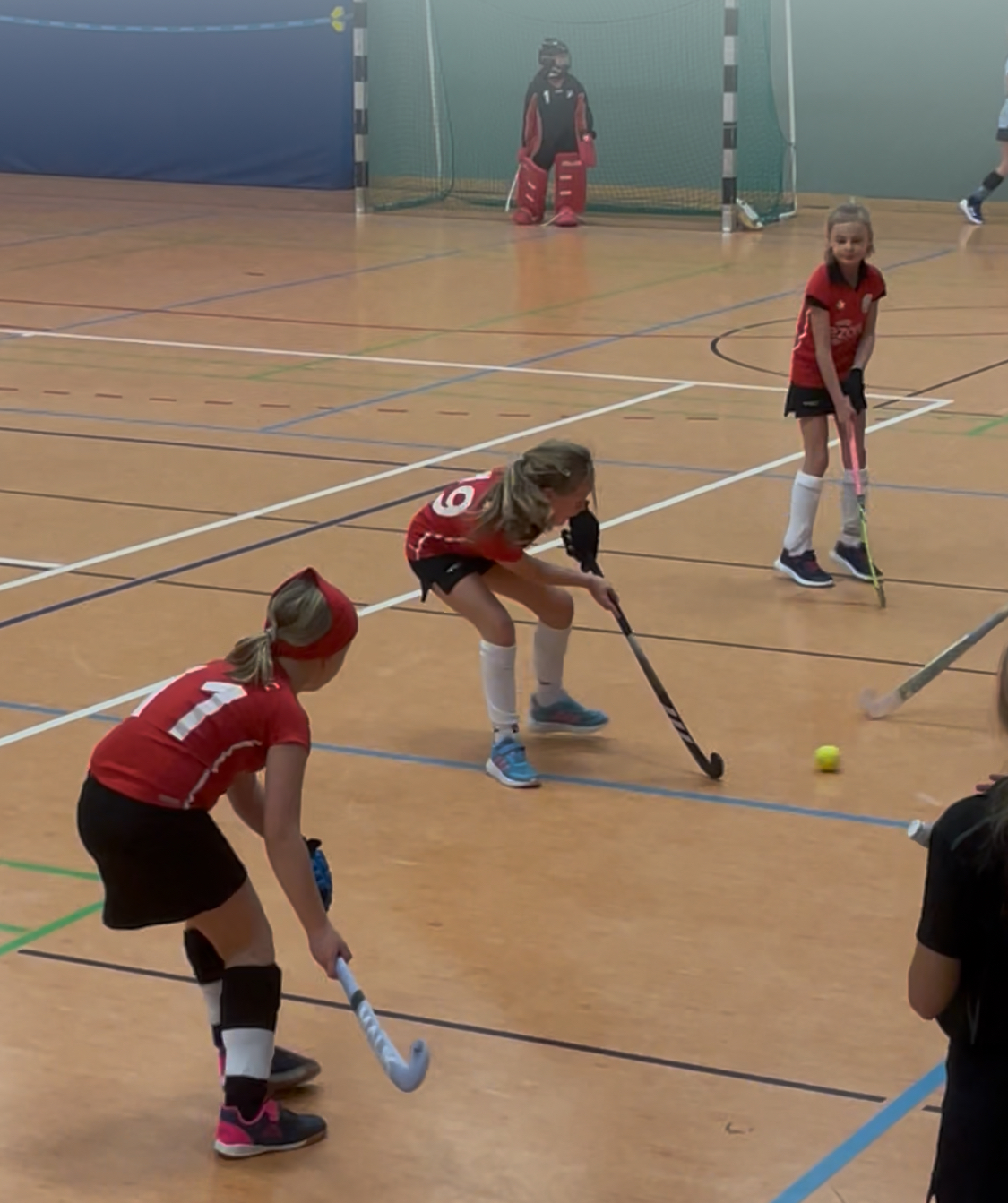 Kinder spielen in der Turnhalle Hockey.