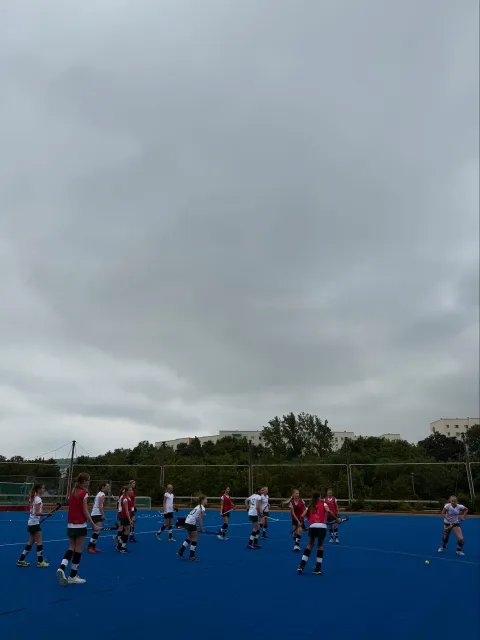 Hockeyspieler in roten Trikots auf Hockeyfeld unter bewölktem Himmel.