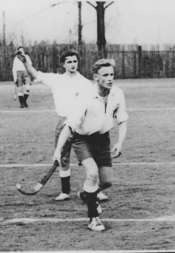 Zwei Männer spielen Feldhockey auf einem Rasenplatz.