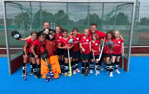 Mannschaft in roten Trikots und orangefarbenen Hosen vor Tor.