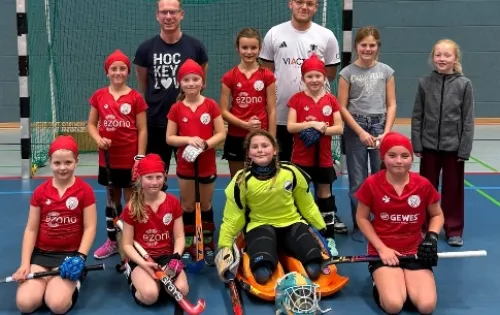 Mannschaftsfoto von Hockeyteam mit Kindern und Erwachsenen in roten Trikots.