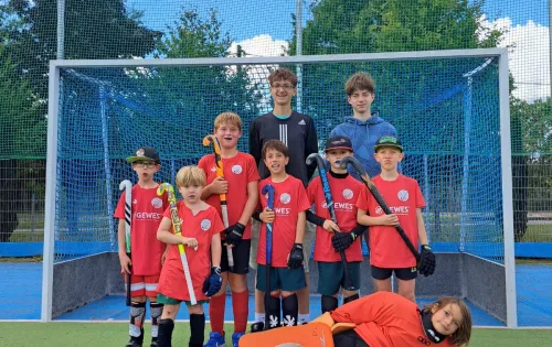 Mannschaft in roten Trikots vor Hockeytor auf Kunstrasenplatz im Sommer.