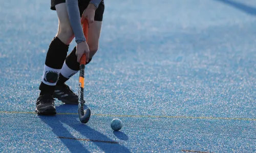 Nahaufnahme einer Feldhockey-Spielerin, die auf blauem Kunstrasen den Ball mit dem Schläger führt.