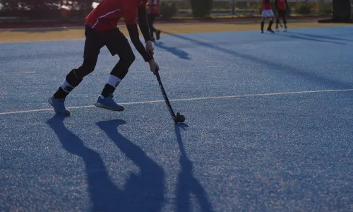 Hockey-Spieler auf blauem Kunstrasen, hält Hockeyschläger im am Ball.